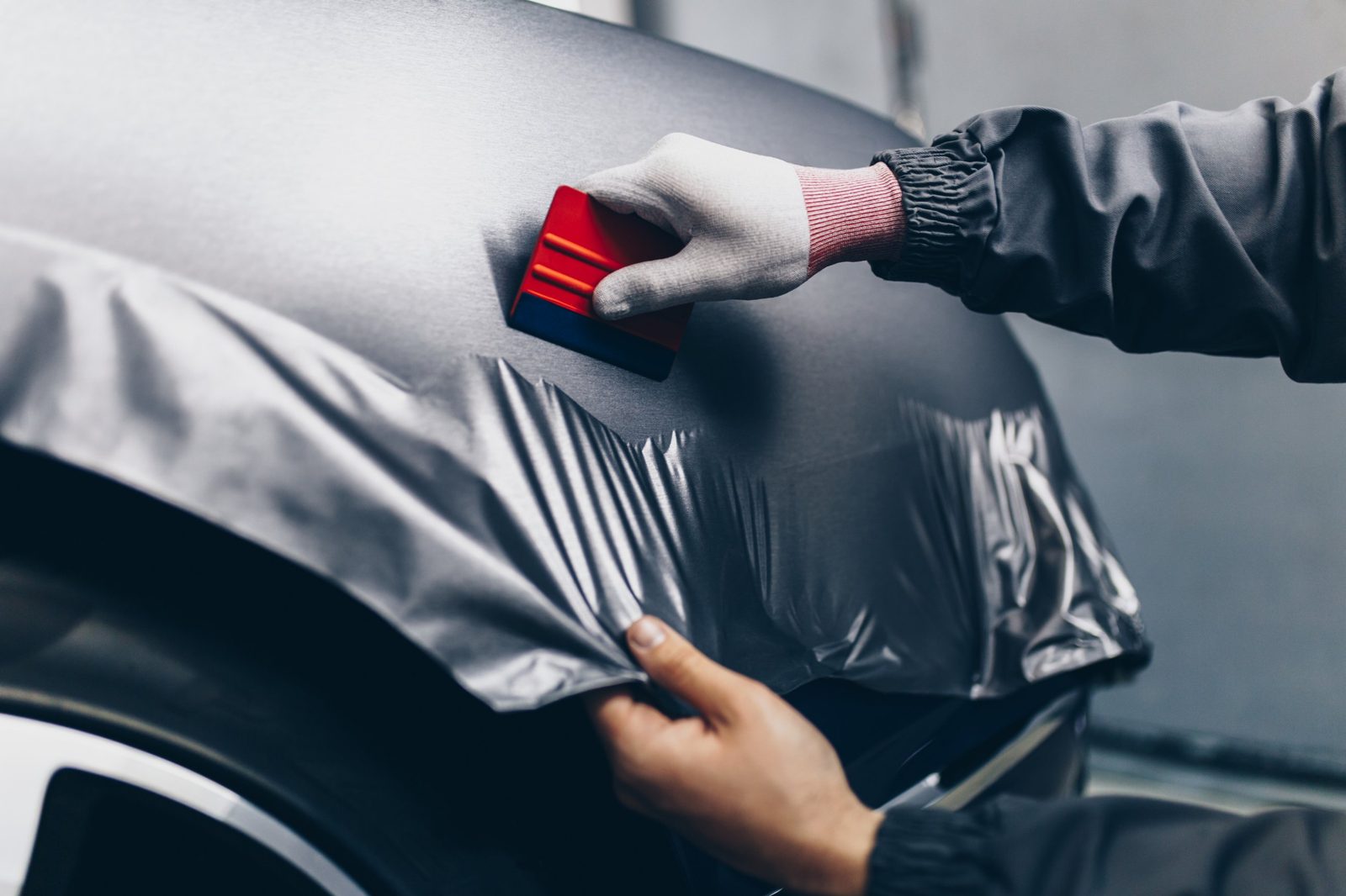 Gray vinyl wrap being smoothed onto a car with a squeegee